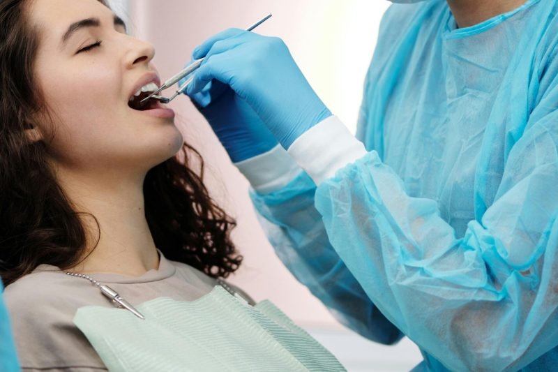 Dentist in protective gear examining a woman's teeth during a dental clinic visit.
